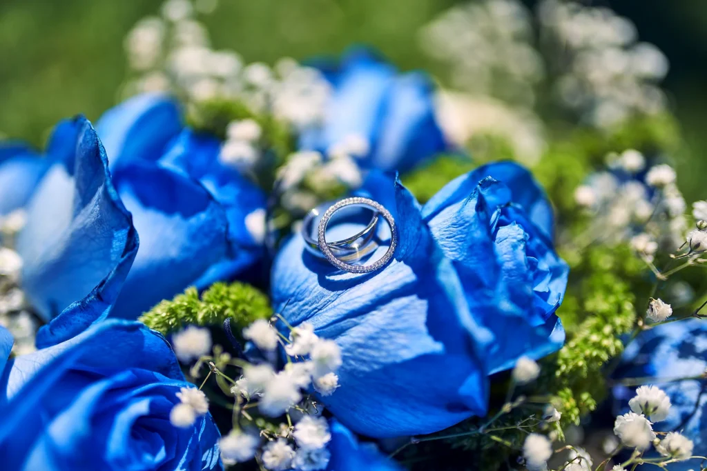 Artistic wedding photo of his and hers wedding bands glistening in the sun laying against a wedding bouquet