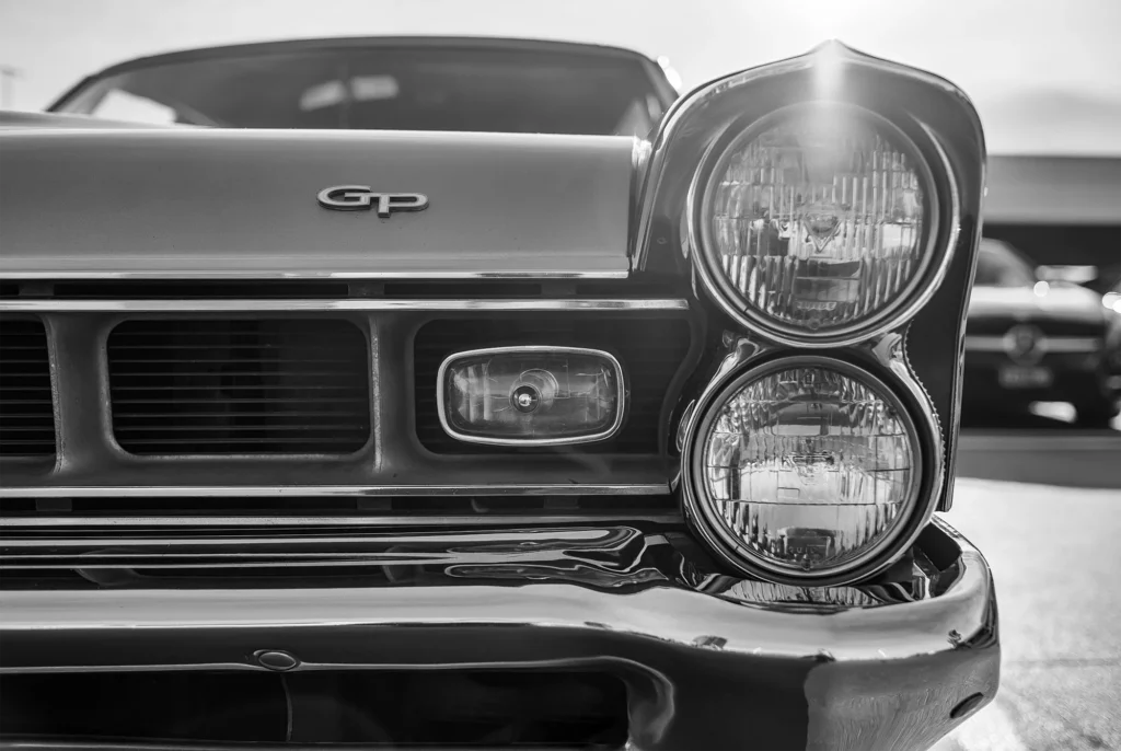 Sarasota automotive photography of classic Pontiac GTO front grille and dual headlights in black-and-white, vintage car close-up with sun flare for local dealership marketing.