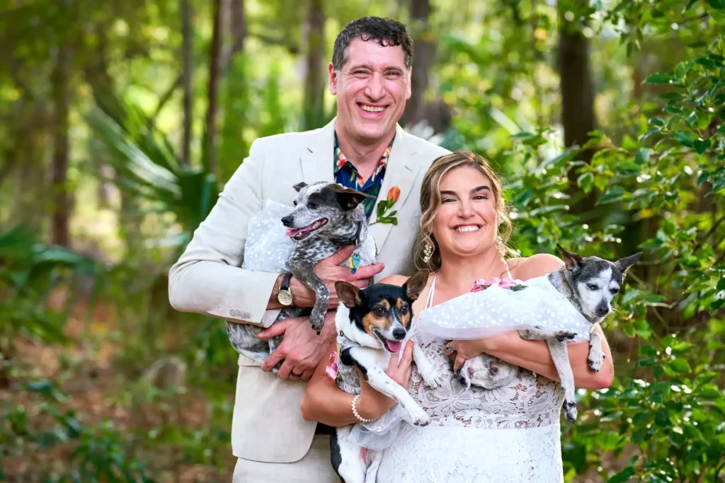 Wedding day portrait photograph of bride and groom smiling and holding their pet dogs