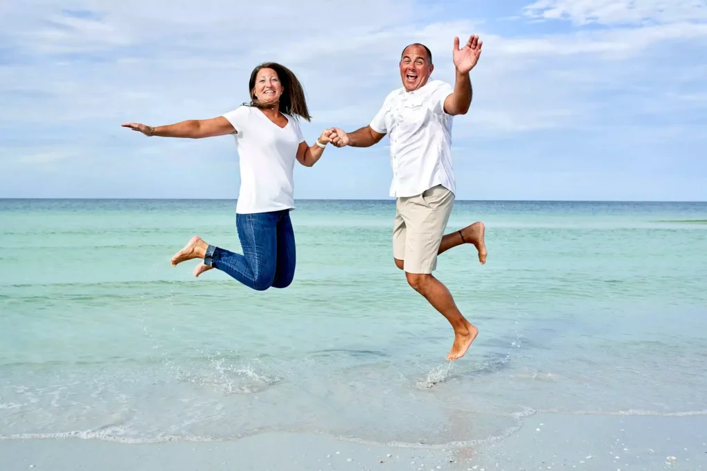 Husband and wife jumping in Siesta Key beach family portrait session