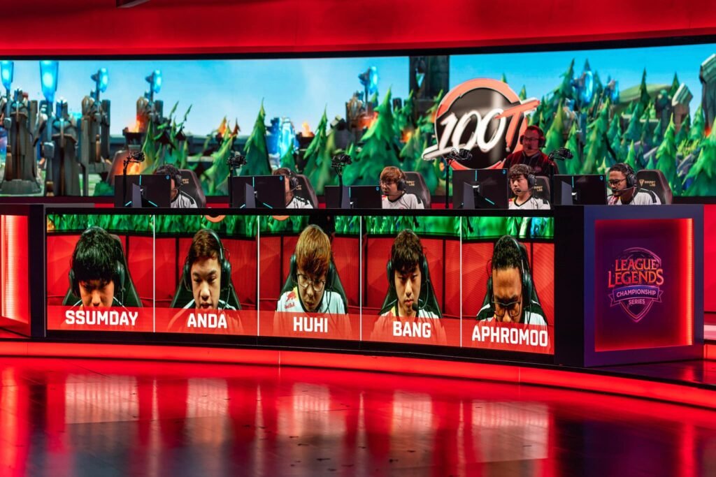 Teammates photographed competing together in front of video gaming monitors at live event - League of Legends