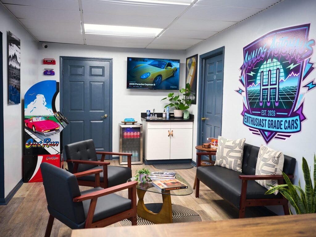 Analog Autohaus Sarasota office lounge with OutRun arcade cabinet, retro neon logo wall mural, mid-century leather seating and glass coffee table. Photo by Thru My Eyes Productions.