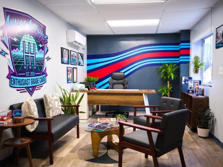 Analog Autohaus Sarasota office with hand-painted blue and red racing stripe mural behind wood desk, neon logo wall and mid-century seating. Photo by Thru My Eyes Productions.