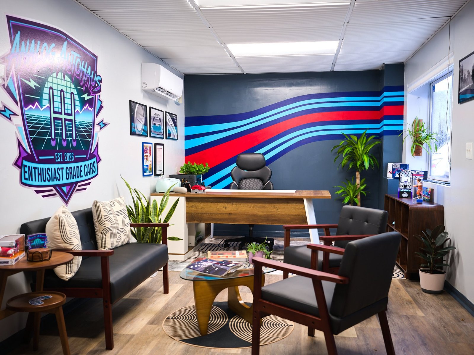 Analog Autohaus Sarasota office with hand-painted blue and red racing stripe mural behind wood desk, neon logo wall and mid-century seating. Photo by Thru My Eyes Productions.