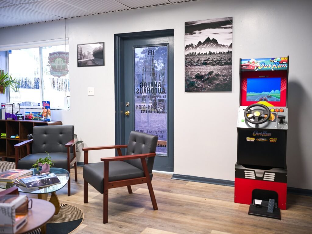 Analog Autohaus Sarasota office entrance with OutRun arcade cabinet, black-and-white fine-art mountain print by Nicholas and mid-century chairs. Photo by Thru My Eyes Productions.