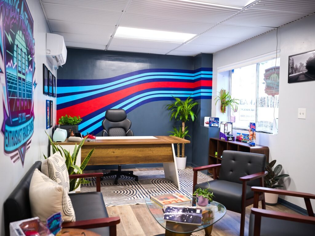 Analog Autohaus Sarasota office desk area with hand-painted racing stripe mural, neon logo wall, plants and mid-century lounge chairs. Photo by Thru My Eyes Productions.
