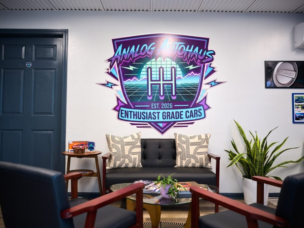 Analog Autohaus Sarasota retro neon Enthusiast Grade Cars logo wall mural above mid-century leather loveseat and glass coffee table. Photo by Thru My Eyes Productions.