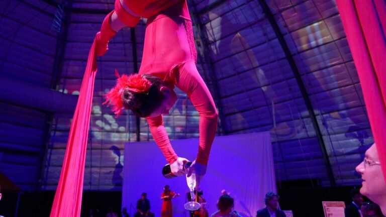 Aerialist in red pouring champagne upside down at the Senior Friendship Centers City of Lights Gala, filmed by Thru My Eyes Productions